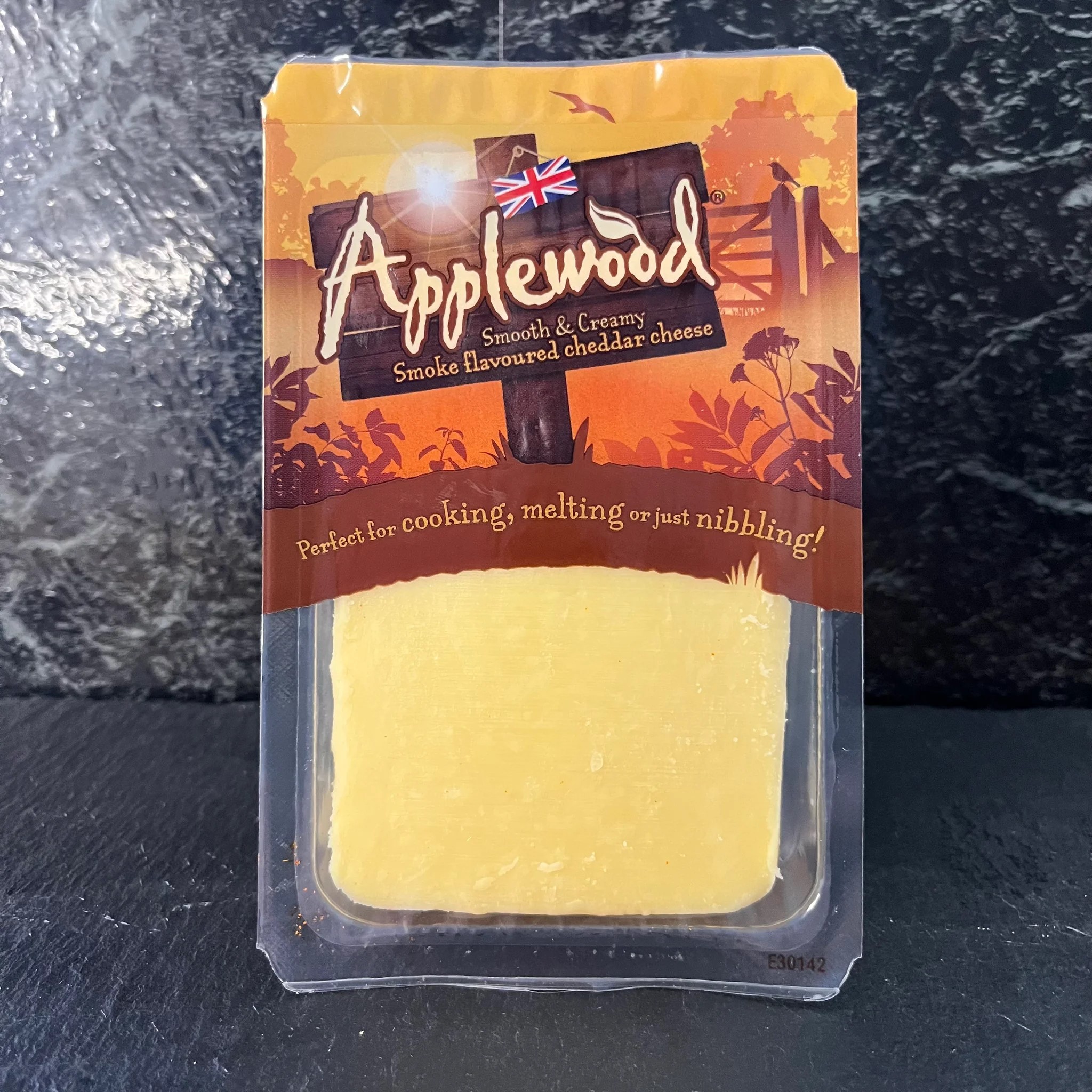 A rectangular slice of Applewood cheddar packed in a plastic carton, placed against black marble