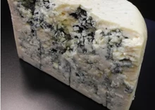 A half-cut wheel of Big Rock Blue cheese, showcasing its ivory-colored interior with blue veins, is set against a dark grey background
