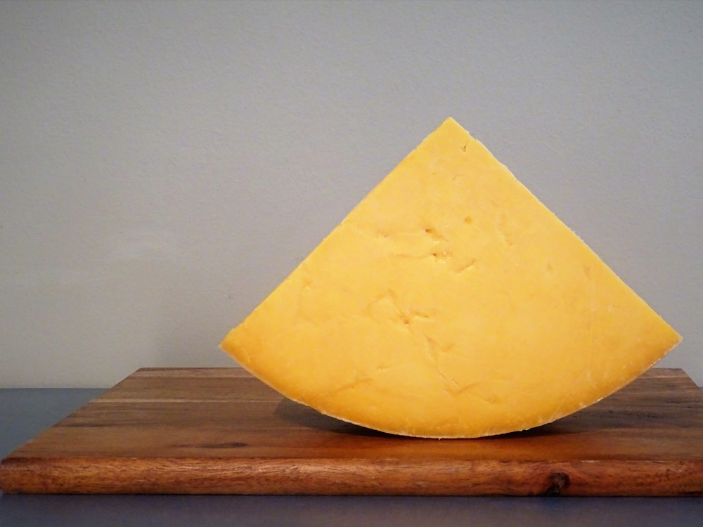 A triangular piece of Auld Lochnagar cheese revealing orange interior  placed on a wooden cutting board