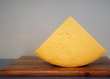 A triangular piece of Auld Lochnagar cheese revealing orange interior  placed on a wooden cutting board