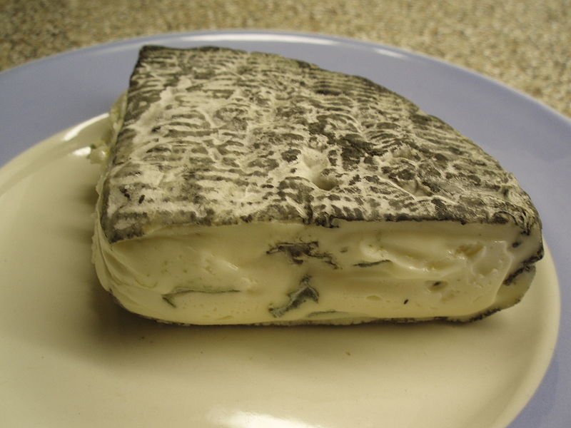 A large piece of Rochebaron, showcasing its ash-coated rind and blue veins, sits on a white plate.