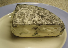 A large piece of Rochebaron, showcasing its ash-coated rind and blue veins, sits on a white plate.