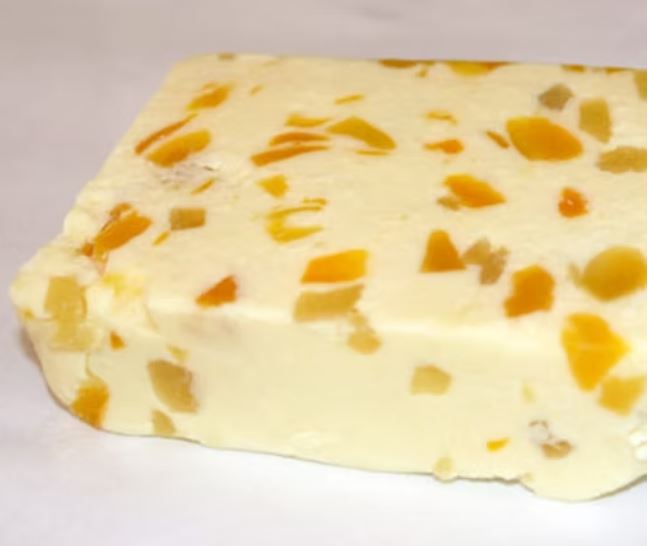 A piece of White Stilton infused with Mango & Ginger cheese, showcasing mango pieces, rests on a grey background.