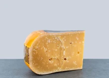 Slice of 3yrs Aged Vintage Gouda cheese with caramel notes and salt crystals, displayed against a grey background