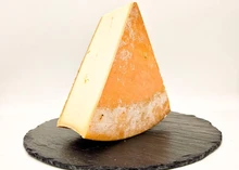 A triangular slice of Abondance cheese sits on a round marble surface, revealing its pale-yellow interior