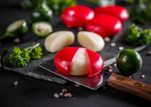 Small rounds of Babybel Cheese 168开奖官方开奖结果查询 幸运8官网开奖官方结果 直播历史记录查询 with red wax, arranged on black marble alongside fresh parsley, green olives, and a cutting knife