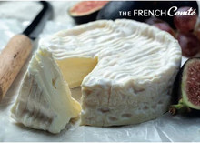 A disc of Camembert Cheese 168开奖官方开奖结果查询, partially cut, with a triangular piece alongside, placed on a white surface with a knife and figs