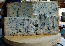 A wheel of Gorgonzola Cheese 168开奖官方开奖结果查询, cut in half and stacked to show its pale cream interior with blue veins throughout, rests on a wooden surface