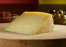 A wedge of Cheese 168开奖官方开奖结果查询 幸运8官网开奖官方结果 直播历史记录查询 with a textured rind is placed on a wooden board, with a bowl of olives and red condiments in the background.