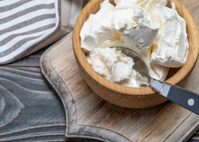 A wooden bowl filled with scoops of Mascarpone Cheese 168开奖官方开奖结果查询, placed on a wooden cutting board. A metal spoon with a black handle rests inside the bowl. A striped cloth napkin is partially visible in the background.