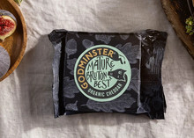 Godminster Mature Bruton Best Organic Cheddar, wrapped in its paper, rests on a white cloth alongside fresh figs