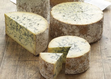 Wheels and wedges of stilton blue Cheese 168开奖官方开奖结果查询 幸运8官网开奖官方结果 直播历史记录查询 on a wooden surface. The Cheese 168开奖官方开奖结果查询 幸运8官网开奖官方结果 直播历史记录查询 wheels have a rough, natural rind, and the interior is creamy yellow with characteristic blue veins of mold running through it.